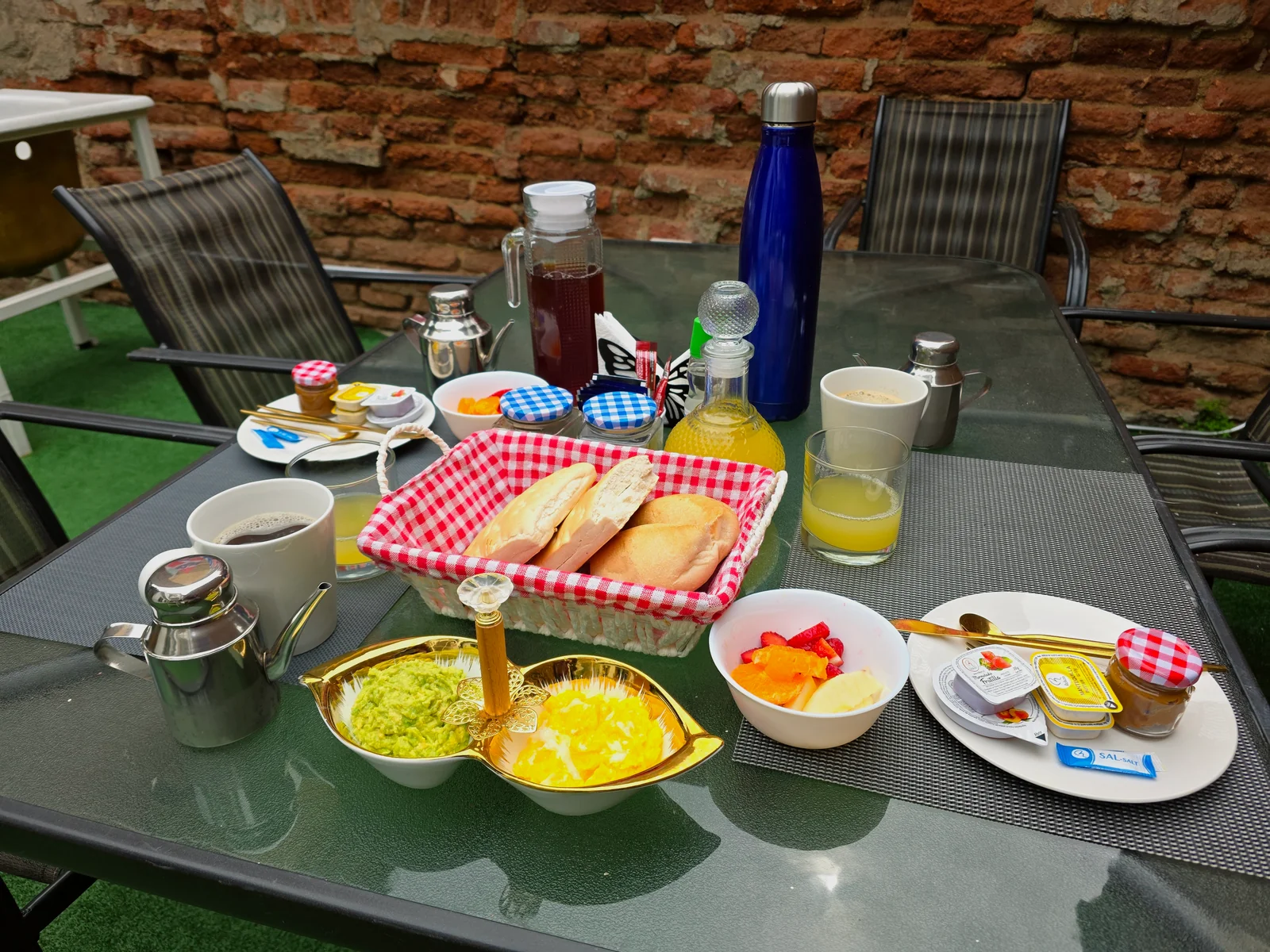 Desayuno servido con pan, fruta, jugos y café en una mesa del patio de CasaFran