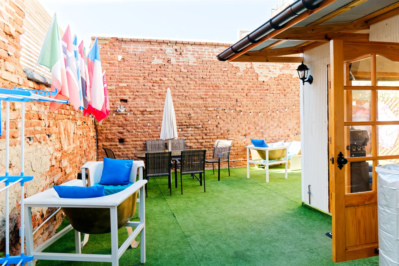 Patio trasero de CasaFran con banderas, mesas y sillones junto a muros de ladrillo